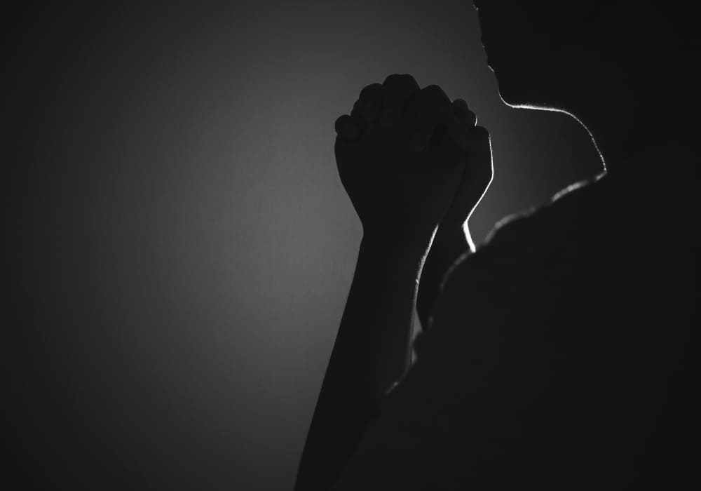 A black-and-white silhouette of a person with hands clasped in prayer, emanating a serene and reflective atmosphere.