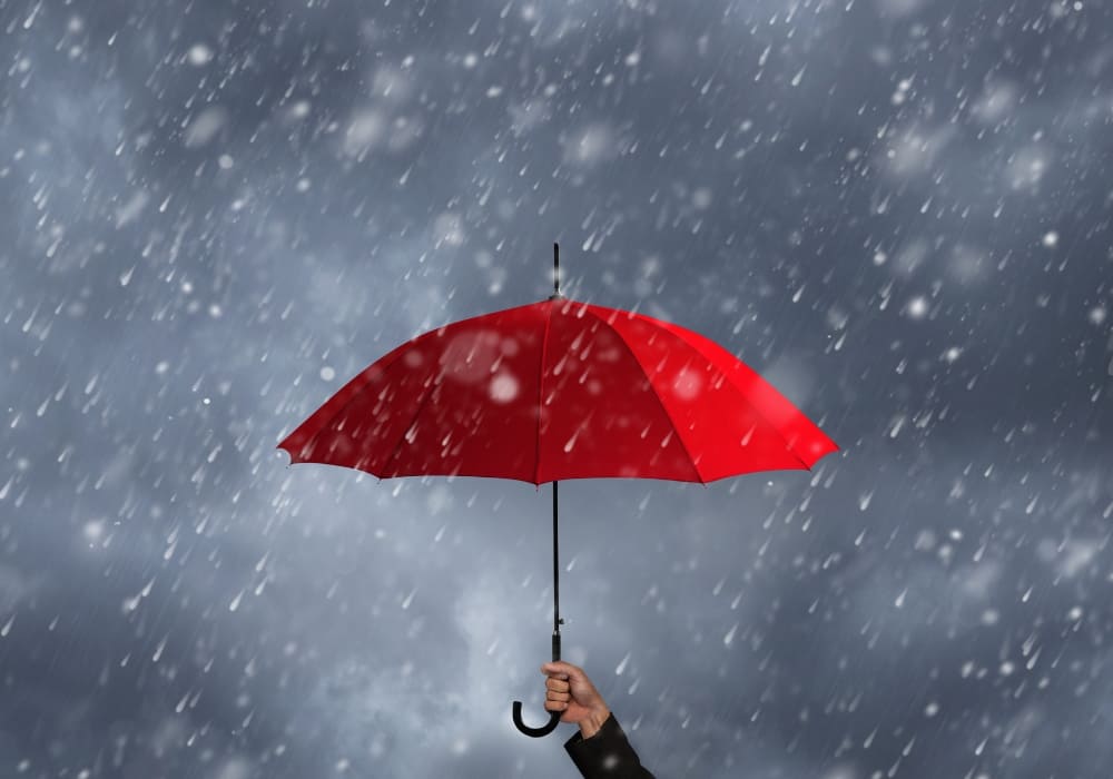 A striking image of a hand holding a vibrant red umbrella against a backdrop of heavy rainfall and dark, stormy skies.