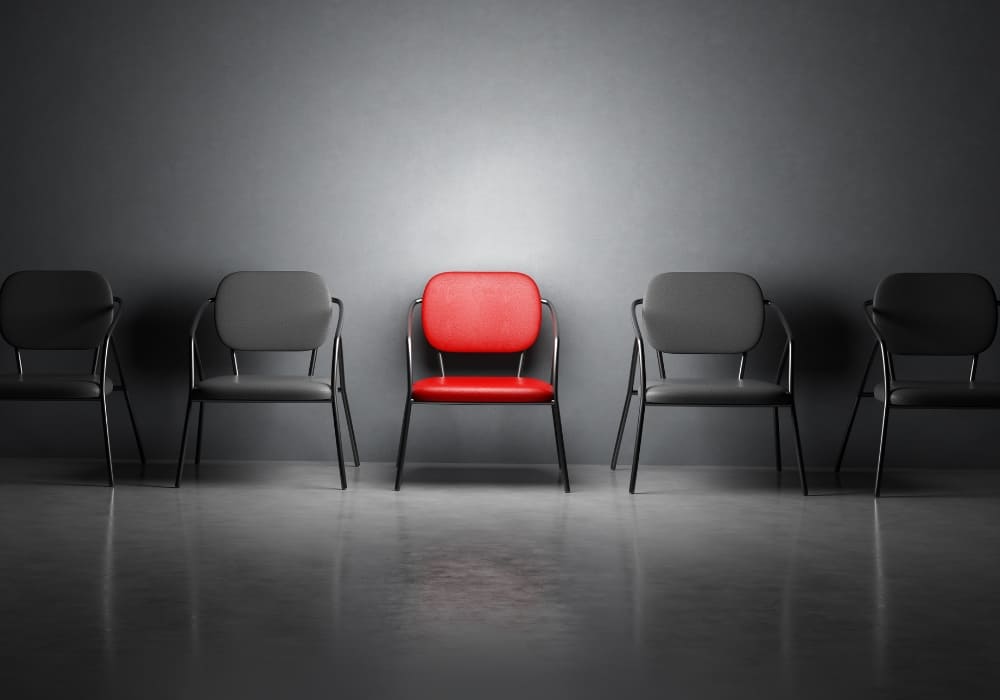 A row of black chairs with a single red chair standing out in the center.